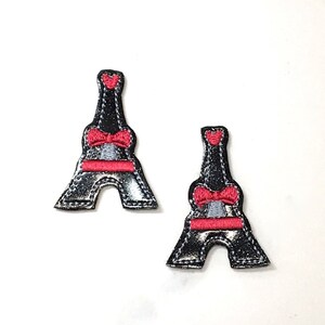 May include: Two black and silver glitter Eiffel Tower patches with a red bow and a red heart on top.