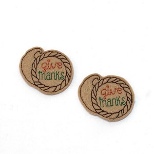 May include: Two brown felt ornaments with a rope design and the text "give thanks" in green and orange embroidery.