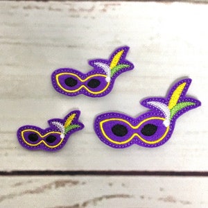 May include: Three purple felt Mardi Gras masks with yellow trim and green and white feathers. The masks are different sizes.