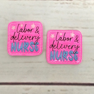 Puede incluir: Dos parches de tela rosa con costuras blancas. Cada parche tiene el texto "Labor & Delivery Nurse" en letra cursiva negra con letras bordadas azules. Los parches tienen estrellas bordadas blancas.