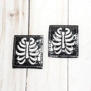 Könnte beinhalten: Zwei schwarze und weiße Bügelbilder mit Glitzer-Finish. Jedes Bügelbild zeigt ein weißes Rippenknochen-Design.