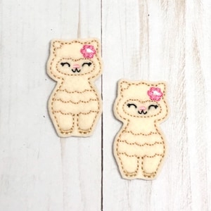 May include: Two felt appliques of a white llama with a pink flower on its head. The llamas have a smiling face with closed eyes and a gold embroidered outline.