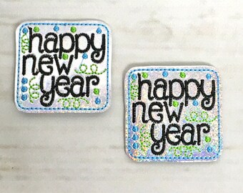 Puede incluir: Dos parches bordados de forma cuadrada con fondo blanco y detalles en azul y verde. Los parches dicen "happy new year" en letras negras.