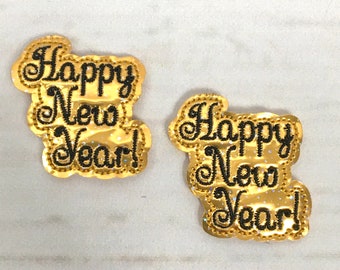 Puede incluir: Dos parches termoadhesivos de color dorado brillante con bordado negro que dicen "Happy New Year!"