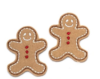 May include: Two brown felt gingerbread man ornaments with white stitching and red button details.
