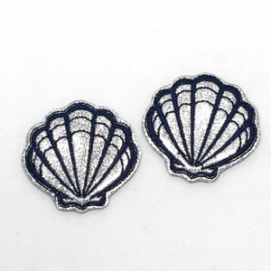 May include: Two silver glitter seashells with a navy blue outline. The shells are flat and have a slightly raised design.