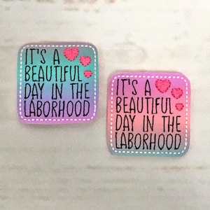 Puede incluir: Dos parches termoadhesivos cuadrados con un fondo degradado de arcoíris. Los parches tienen costuras blancas alrededor de los bordes y dicen "It's a beautiful day in the laborhood" con corazones rosas.