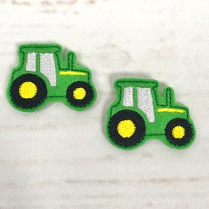 May include: Two green felt tractor appliques with black wheels and yellow centers. The tractors have white windows and yellow details.