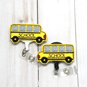 Può includere: Due porta badge retrattili a tema scuolabus giallo con lacci neri e bianchi. L'autobus ha la scritta "SCHOOL" stampata sul lato.
