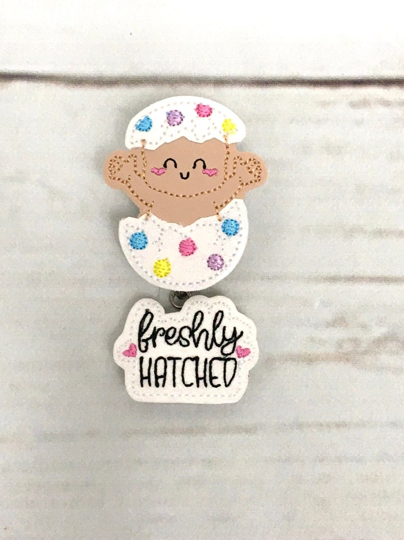 This listing is for baby in an egg with freshly hatched Badge Reel. The badge reel is made with a baby hatching egg feltie stitched on white glitter vinyl backed with felt The freshly hatched word feltie is on white glitter vinyl is backed with felt