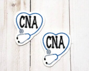 May include: Two white heart-shaped patches with blue outlines. Each patch has a black embroidered stethoscope and the text "CNA" in black.