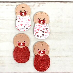 Puede incluir: Cuatro adornos con forma de bebé. Dos tienen pañales blancos con corazones rosas y marrones. Los otros dos tienen pañales de purpurina roja. Cada uno tiene una cabeza de color canela con un diseño de pelo rizado y ojos cerrados.