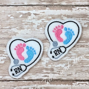 May include: Two white felt heart-shaped patches with embroidered baby footprints and a stethoscope with the letters "RN" on it.