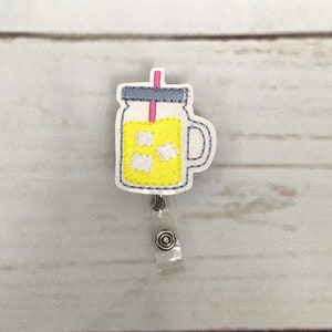 May include: A yellow mason jar with a pink straw and ice cubes, attached to a clear plastic badge holder with a silver clip.