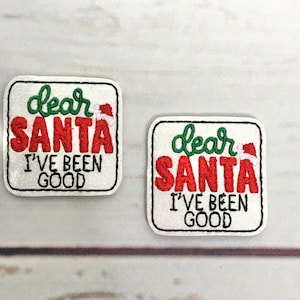 Può includere: Due toppe quadrate con la scritta "dear SANTA I'VE BEEN GOOD". La parola "dear" è in verde, "SANTA" in lettere rosse e "I'VE BEEN GOOD" in nero. Un piccolo cappello di Babbo Natale è sopra la lettera "A".