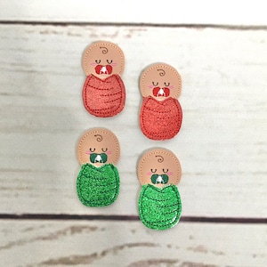 Puede incluir: Cuatro aplicaciones de bebé de fieltro, dos en rojo y dos en verde. Cada aplicación presenta un bebé con un chupete y una postura de dormir enroscado.