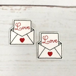 May include: Two white embroidered patches with a red heart and the word "Love" on a white background. The patches are on a white wooden surface.