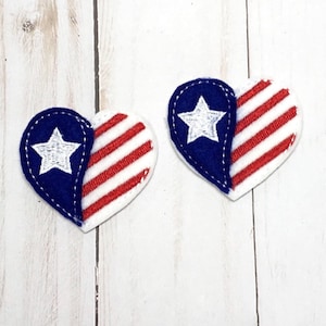 Puede incluir: Dos parches de fieltro en forma de corazón con un diseño de bandera estadounidense roja, blanca y azul. Un corazón tiene una sección azul con una estrella blanca, y el otro corazón tiene una sección de rayas rojas y blancas.