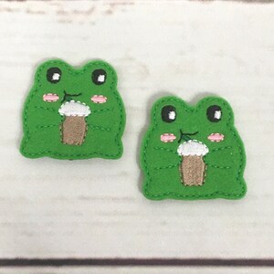 以下が含まれることがあります： 黒い目とピンクの頬、白と茶色のアイスクリームコーンを持つ、緑のフェルト製のカエルのアップリケが2つです。