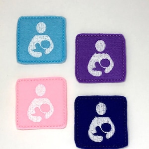 Puede incluir: Cuatro parches de fieltro con una imagen bordada en blanco de una persona sosteniendo un bebé. Los parches son de color azul, morado, rosa y azul oscuro.