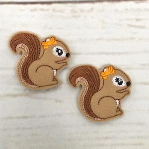 May include: Two brown felt appliques of squirrels with orange accents. The squirrels are facing different directions and have embroidered details.