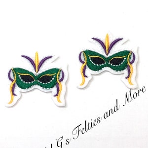May include: Two embroidered Mardi Gras mask patches. Each mask is green, black, purple, and gold, with white trim. The text "Mel G's Felties and More" is in the lower right corner.