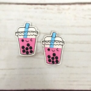 May include: Two pink embroidered patches of a boba tea cup with a blue straw and black boba pearls. The cups have a smiling face.