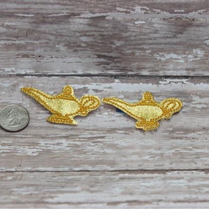 May include: Two gold-colored genie lamp iron-on patches. The patches are about the size of a US quarter.