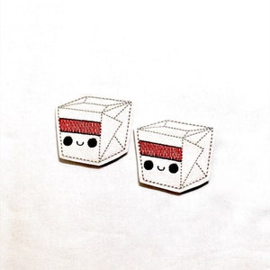 May include: Two white, cube-shaped patches with a red stripe and smiling faces. The patches have black eyes and a stitched outline. The patches are on a white background.