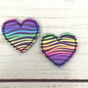 May include: Two rainbow zebra print heart-shaped patches with black stitching around the edges.