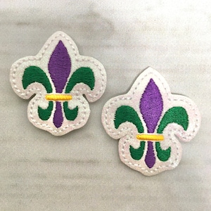 May include: Two embroidered fleur-de-lis patches in purple, green and gold.