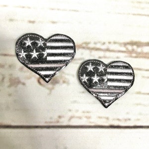 May include: Two black and white heart-shaped patches with an American flag design. The patches have a distressed look and are made of fabric.