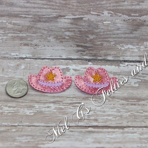 Puede incluir: Dos sombreros de vaquero de fieltro rosa con una estrella dorada y ribete morado. Los sombreros son aproximadamente del tamaño de una moneda de 25 centavos de dólar estadounidense.