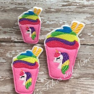 May include: Three felt unicorn slushie patches in different sizes. The slushies are pink with rainbow swirls and topped with a yellow straw. The unicorn faces are embroidered in rainbow colors.
