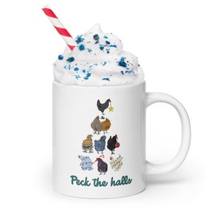May include: White ceramic mug with a Christmas tree design featuring chickens wearing festive lights and ornaments. The mug has the text "Peck the halls" on the bottom. The mug is topped with whipped cream and blue sprinkles.