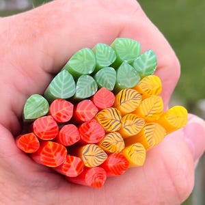 May include: A collection of glass rods with leaf designs in green, orange, and yellow colors. The rods are arranged in a stack, with the green rods at the top, the orange rods in the middle, and the yellow rods at the bottom.