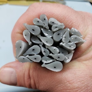 May include: A bundle of gray, teardrop-shaped objects with a small black dot on each. The objects are held in a hand, and appear to be made of a translucent material. The ends are cut, revealing a layered texture.
