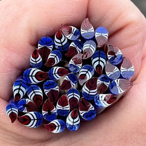May include: A collection of red, white, and blue glass beads with a feather design. The beads are teardrop shaped and have a glossy finish.