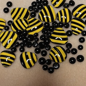 May include: A collection of black and yellow striped glass tiles and black glass beads. The tiles are shaped like bee wings and the beads are round.