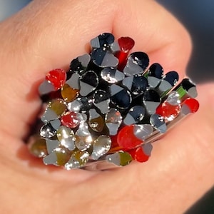 May include: A bundle of glass rods in various colors, including red, black, silver, and green. The rods are bundled together and have a shiny, reflective surface.