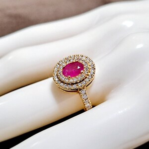 May include: A gold ring featuring a large oval ruby set within a double halo of smaller diamonds.