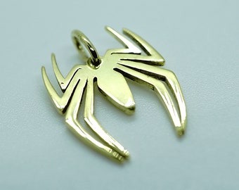 Pode incluir: Um pingente de aranha de metal dourado. A aranha é estilizada e tem um design simples.