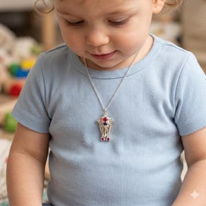 May include: A silver pendant necklace with a detailed design, featuring red and blue gemstones. The necklace is worn on a light blue t-shirt.