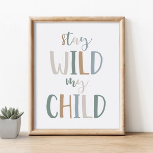 May include: A framed print with the words "Stay WILD my CHILD" in a playful font. The text is in shades of brown, blue, and green. A small potted succulent sits to the left of the frame, on a wooden surface.