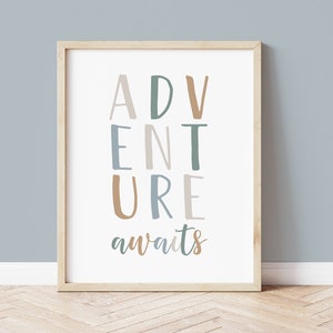 May include: A framed print with the words "ADVENTURE awaits" in a playful font. The letters are in shades of blue, green, and brown against a white background. The frame is a light wood color, and the print is displayed against a blue wall.
