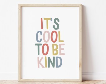 May include: A framed art print with the words "IT'S COOL TO BE KIND" in colorful, playful lettering. The text is in a variety of colors, including red, yellow, blue, and pink. The frame is a light wood color, and the background is white.