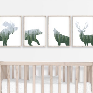 May include: Four framed art prints featuring forest animal silhouettes: a moose, bear, wolf, and deer. Each animal is filled with a green and gray forest scene. The prints are displayed above a light-colored wooden crib.
