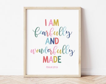 May include: A framed print with the words "I AM fearfully AND wonderfully MADE" in colorful script. The text is set against a white background, with the Bible verse Psalm 139:14 at the bottom. The frame is a light wood color.