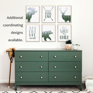 May include: A dark green dresser with six drawers and gold knobs is below six framed art prints. The prints feature forest animal silhouettes and phrases like "LITTLE MAN CAVE" and "ADVENTURE AWAITS". Additional coordinating designs are available.