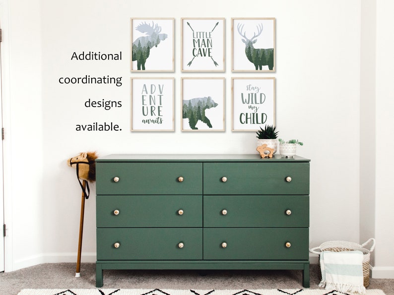 May include: A dark green dresser with six drawers and gold knobs is below six framed art prints. The prints feature forest animal silhouettes and phrases like "LITTLE MAN CAVE" and "ADVENTURE AWAITS". Additional coordinating designs are available.